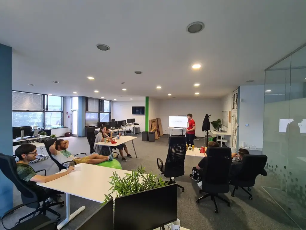 Open-plan office with people working at desks and a meeting table near the entrance